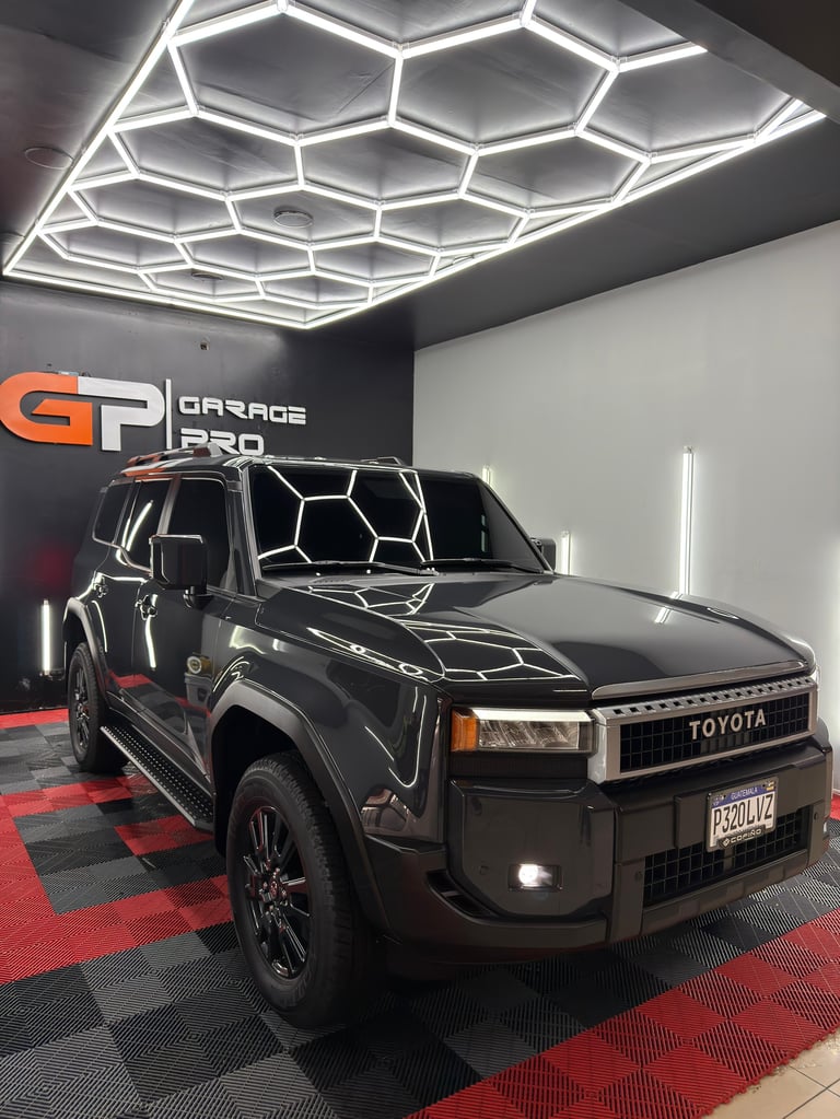 Black Toyota pickup truck displayed in modern garage showroom with honeycomb ceiling lights and red/black checkered flooring