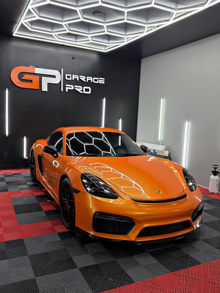 Bright orange Porsche sports car on display in modern garage showroom with geometric ceiling lights and checkered flooring