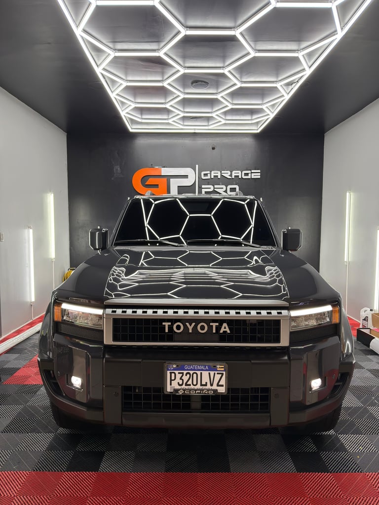 Dark Toyota pickup truck in modern garage with hexagonal neon ceiling lights and Garage P320 signage