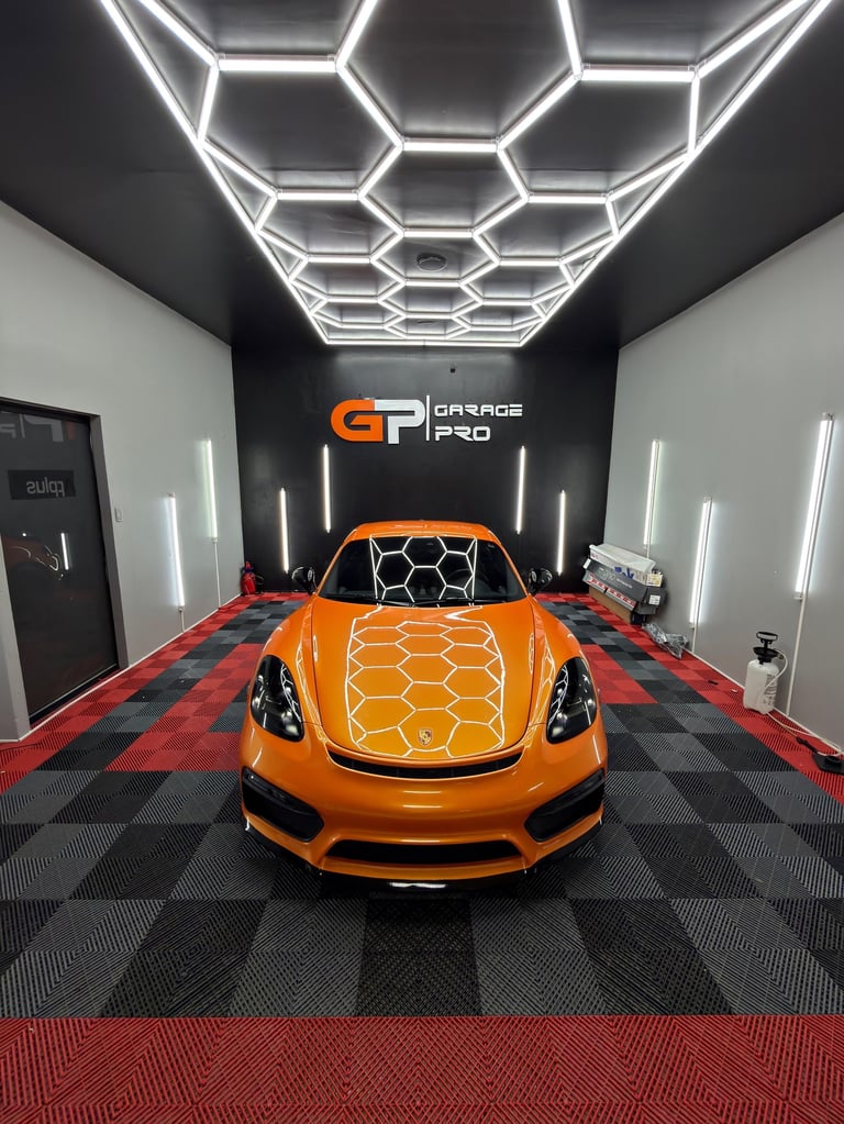 Orange sports car in modern garage with white hexagonal neon ceiling lighting and checkered red black flooring